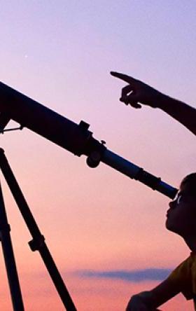 Man and son looking through telescope at dusk