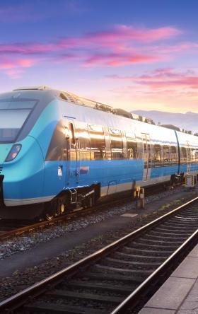 Stock image of a blue passenger train on tracks with pink and purple sunset