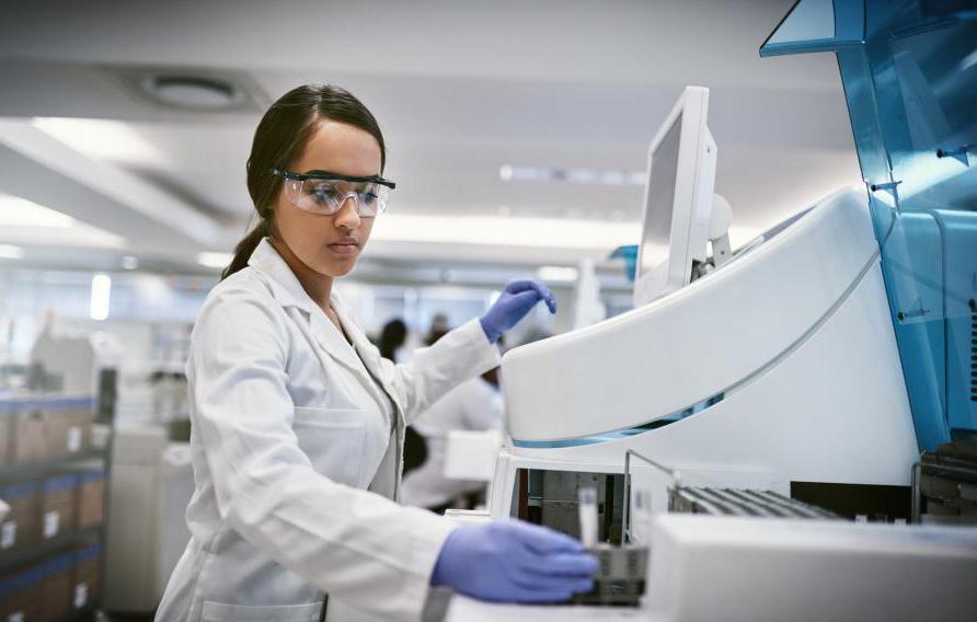 中等皮肤，深色头发，穿着实验服的女人, 安全眼镜和蓝色手套在实验室环境下工作