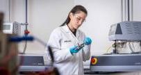 深色头发，身穿白色雅各布斯实验室外套的女士正在实验室设备旁工作
