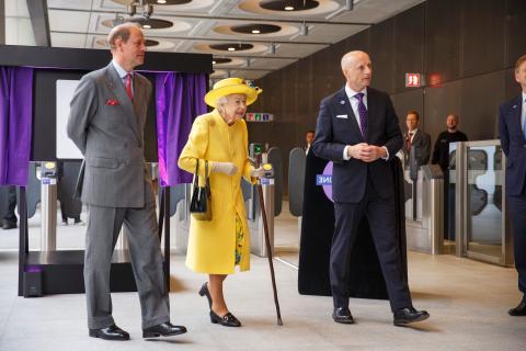 女王陛下身穿黄色外套，头戴黄色帽子，右边是伦敦交通局局长安迪·拜福德，右边是爱德华王子, the Earl of Wessex on her left